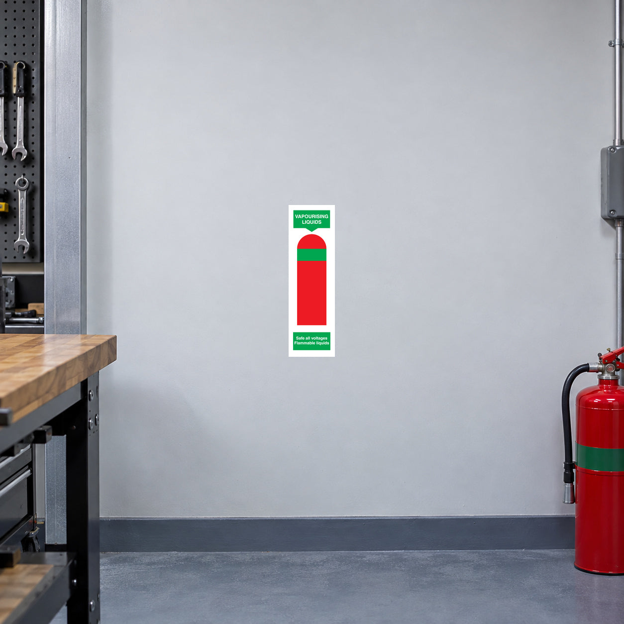 Vaporouising Liquids Fire Extinguisher Sticker applied in a fire-service college equipment demonstration workshop, smooth pale gray wall, unlabelled red demonstration extinguisher with green band far lower right, wooden workbench edge left, blue-gray concrete floor