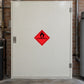 Hazardous Safety Sign Sticker applied in a maintenance fuel storeroom, smooth ivory SINGLE solid steel cabinet door, pipework and brick wall visible at far sides