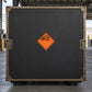 Hazardous Safety Sign Sticker applied in a secure freight inspection station, flat charcoal rigid transit case face with bronze-colored edge hardware, covered depot roof beyond edges