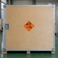 Hazardous Safety Sign Sticker applied in a secure transport packaging room with green floor, flat light brown plywood shipping case front, silver edge rails and recessed latch at far left