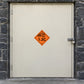 Hazardous Safety Sign Sticker applied in an industrial storage annex, smooth cream SINGLE solid steel door, outer dark stone jamb, padlock at extreme right