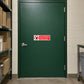 NO Safety Sign Sticker applied in restaurant dry-goods storeroom entrance, solid forest green door, shelves of plain cartons visible at far left