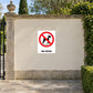 NO Dogs Sign Sticker applied in a cream rendered wall at a municipal garden entrance, stone paving and hedge edges