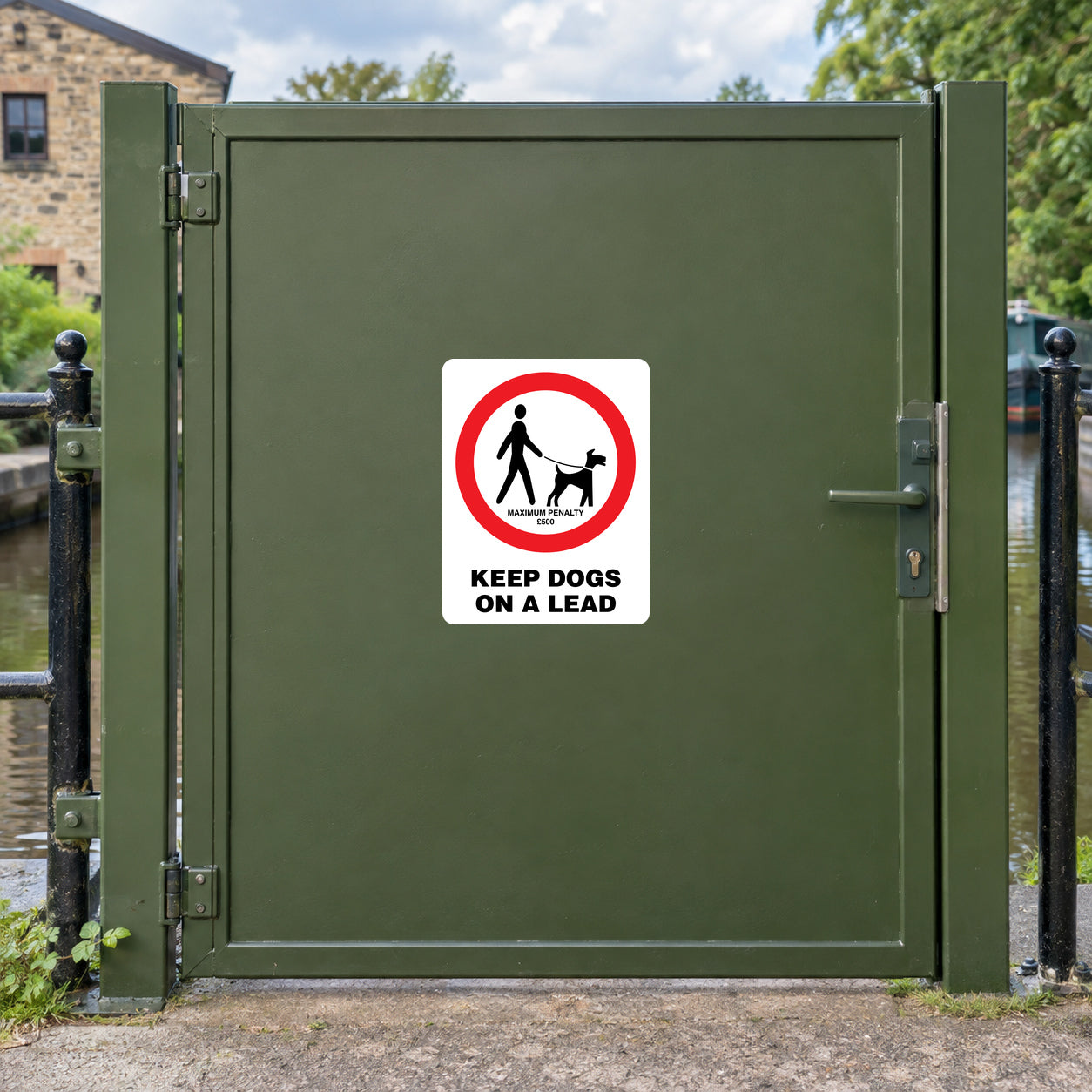 NO Dogs Sign Sticker applied in a solid olive green pedestrian gate beside a canal towpath, canal railing visible only at extreme edges