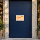 Business Open Closed Sign Sticker applied in a closed ceramics boutique entrance, smooth solid midnight blue door, polished stone jamb and potted fern only at far edges, late afternoon