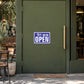 Business Open Closed Sign Sticker applied in an open coffee shop entrance, smooth solid moss green door panel, cafe chairs outside far left and brass pull handle far right, morning daylight