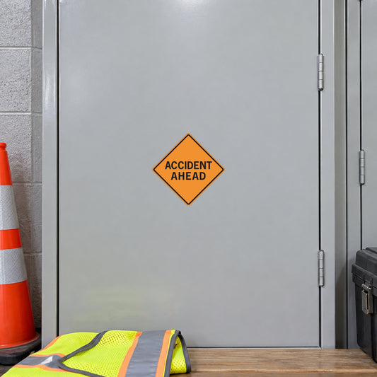 Road sign sticker with yellow diamond warning reading “ACCIDENT AHEAD”