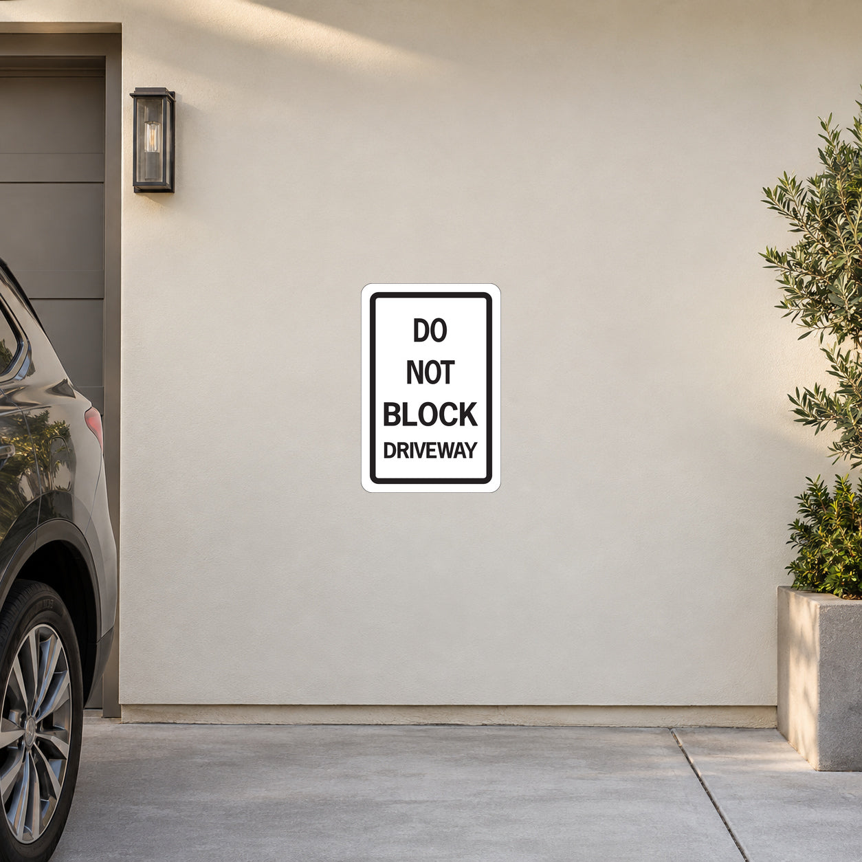 Road Sign Sticker applied in A cream private driveway garage exterior smooth wall with parked car corner far left and shrub planter far right, blank center