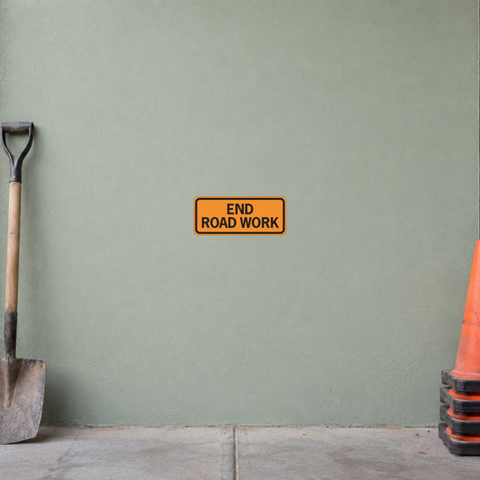 Road Sign Sticker applied in A light sage road service yard smooth wall with cone stack extreme right and shovel extreme left, blank center