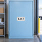 Road sign sticker: white label with black "EAST" text on blue panel