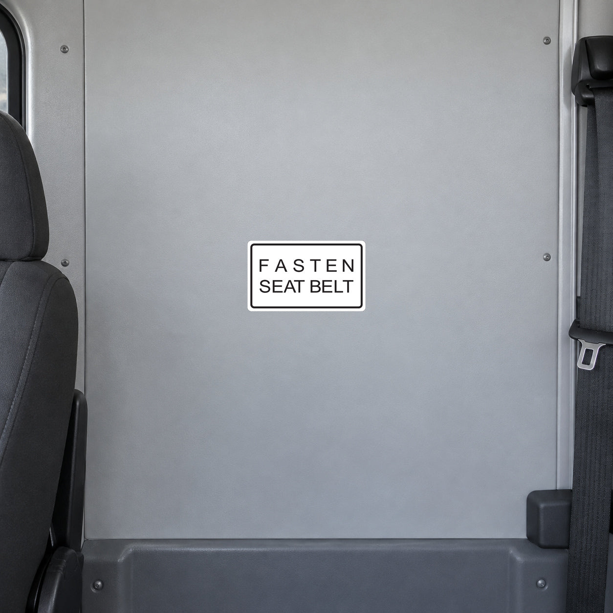 Road Sign Sticker applied in A light grey shuttle bus interior flat smooth partition panel behind driver, seatbelt extreme right and seat edge far left, uninterrupted blank center