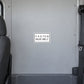 Road Sign Sticker applied in A light grey shuttle bus interior flat smooth partition panel behind driver, seatbelt extreme right and seat edge far left, uninterrupted blank center