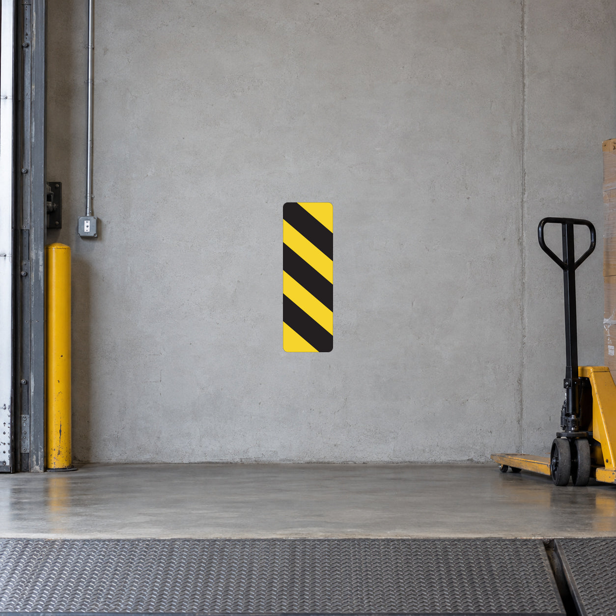 Road Sign Sticker applied in A loading dock equipment room, uninterrupted pale grey concrete wall, pallet jack extreme right and dock threshold bottom