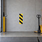 Road Sign Sticker applied in A loading dock equipment room, uninterrupted pale grey concrete wall, pallet jack extreme right and dock threshold bottom