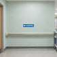 Road Sign Sticker applied in A medical campus service corridor, uninterrupted pale mint painted wall, handrail only below bottom 85 percent and trolley far right