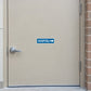 Road Sign Sticker applied in An outpatient clinic side entrance, smooth light sand steel door, handle far left and brickwork extreme right