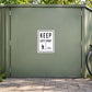 Road Sign Sticker applied in A park cycle storage building, smooth pale moss metal door, bicycle wheel only far right and paving below