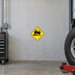 Road Sign Sticker applied in A truck inspection workshop, uninterrupted light grey painted concrete wall, heavy wheel at far right and low red jack below