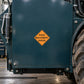 Road Sign Sticker applied in A heavy equipment maintenance bay, smooth dark teal steel service panel, grease gun at extreme left and rugged wheel far right