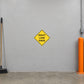 Road Sign Sticker applied in A municipal traffic supply workshop, one continuous smooth light grey painted concrete wall with absolutely no horizontal joints or door panels, orange bollard extreme right and broom extreme left, concrete floor below