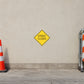 Road Sign Sticker applied in A municipal streetworks store, uninterrupted pale buff concrete wall, road cone extreme left and folded barrier far right
