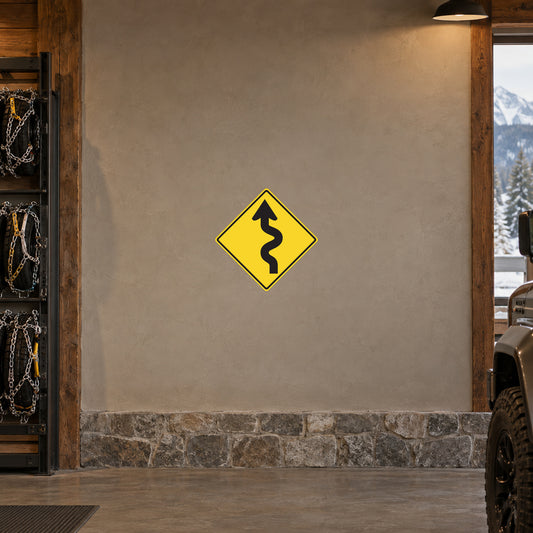 Yellow road warning sticker with black winding-road symbol inside diamond