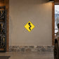 Yellow road warning sticker with black winding-road symbol inside diamond