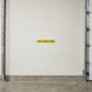 Road Sign Sticker applied in a smooth cream loading bay interior wall, metal measuring pole at far left edge and concrete floor