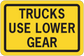 Road sign sticker with yellow background, black border, text "TRUCKS USE LOWER GEAR"