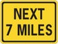 Road sign sticker: yellow "NEXT 7 MILES" warning text with black border