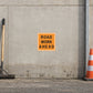 Road Sign Sticker applied in a continuous warm grey road depot wall with an asphalt rake at far left edge and cone at far right
