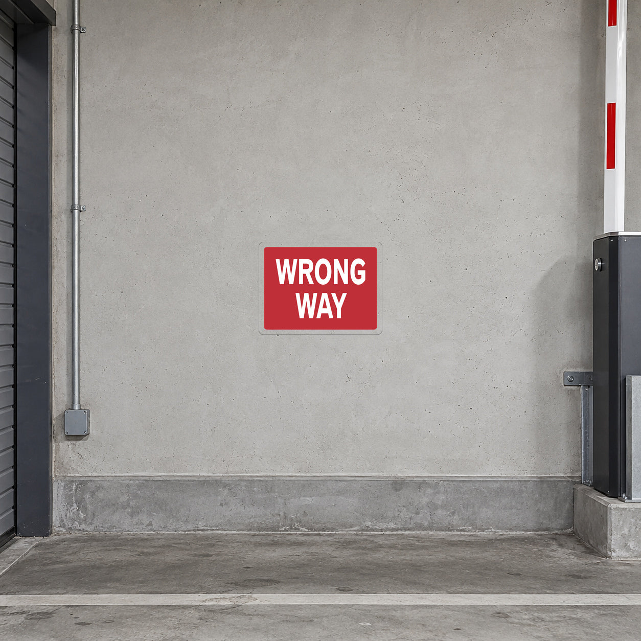 Road Sign Sticker applied in a continuous light grey painted concrete wall at a private parking garage service entrance, barrier mechanism only far right