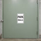 Road Sign Sticker applied in a smooth pale sage parking garage service door, handle at extreme left edge