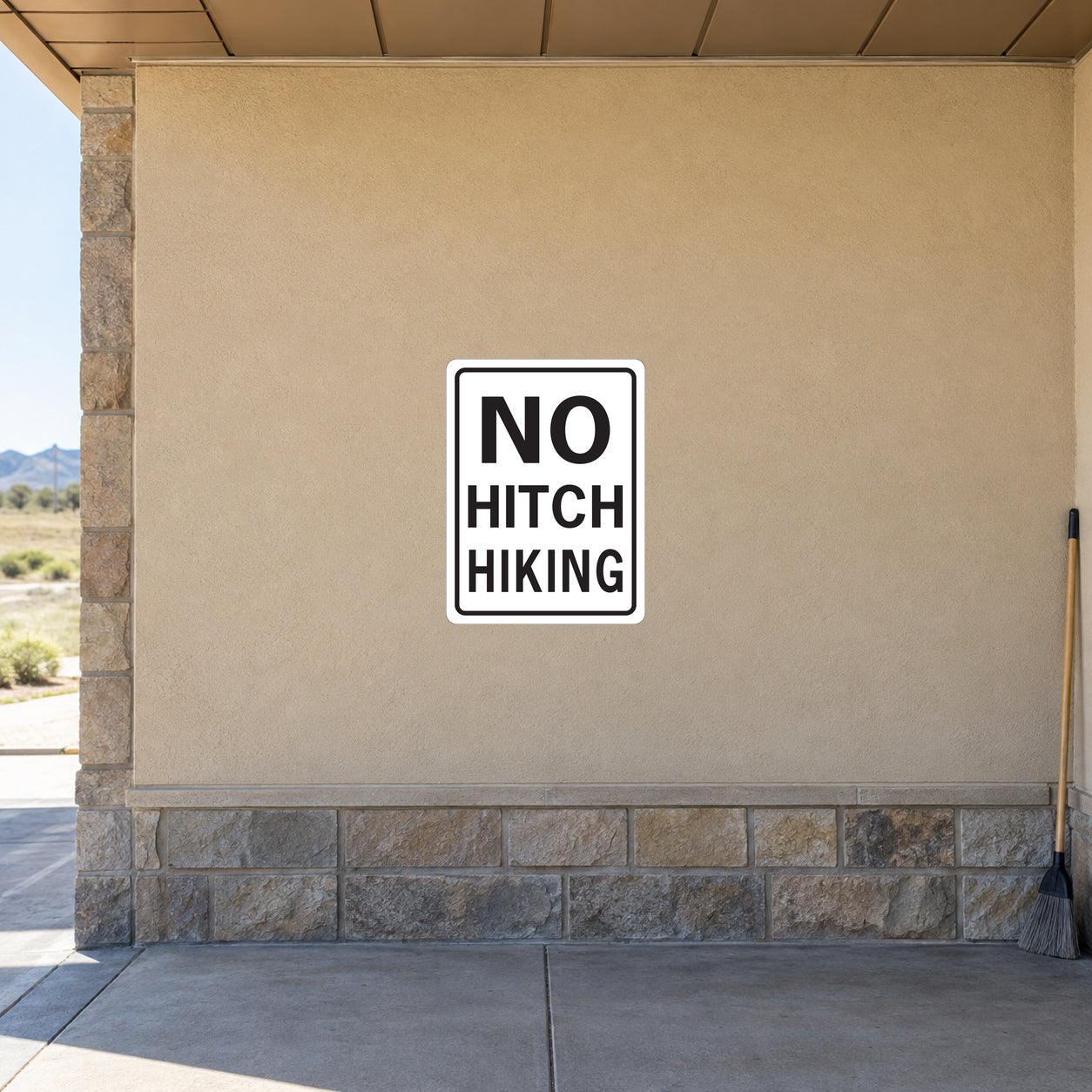 Road Sign Sticker applied in a continuous sandy beige roadside rest facility wall, broom at far right edge
