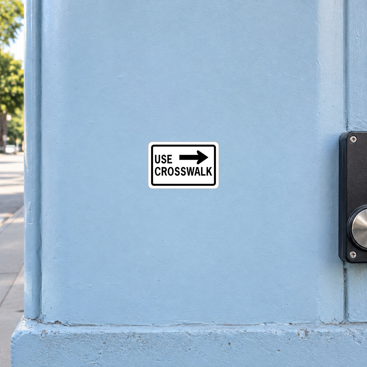 Road Sign Sticker applied in a continuous pale blue pedestrian walkway wall, crossing button housing at far RIGHT edge, blank central surface for right pointing crosswalk instruction