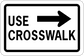 Road sign sticker reading USE CROSSWALK with right arrow