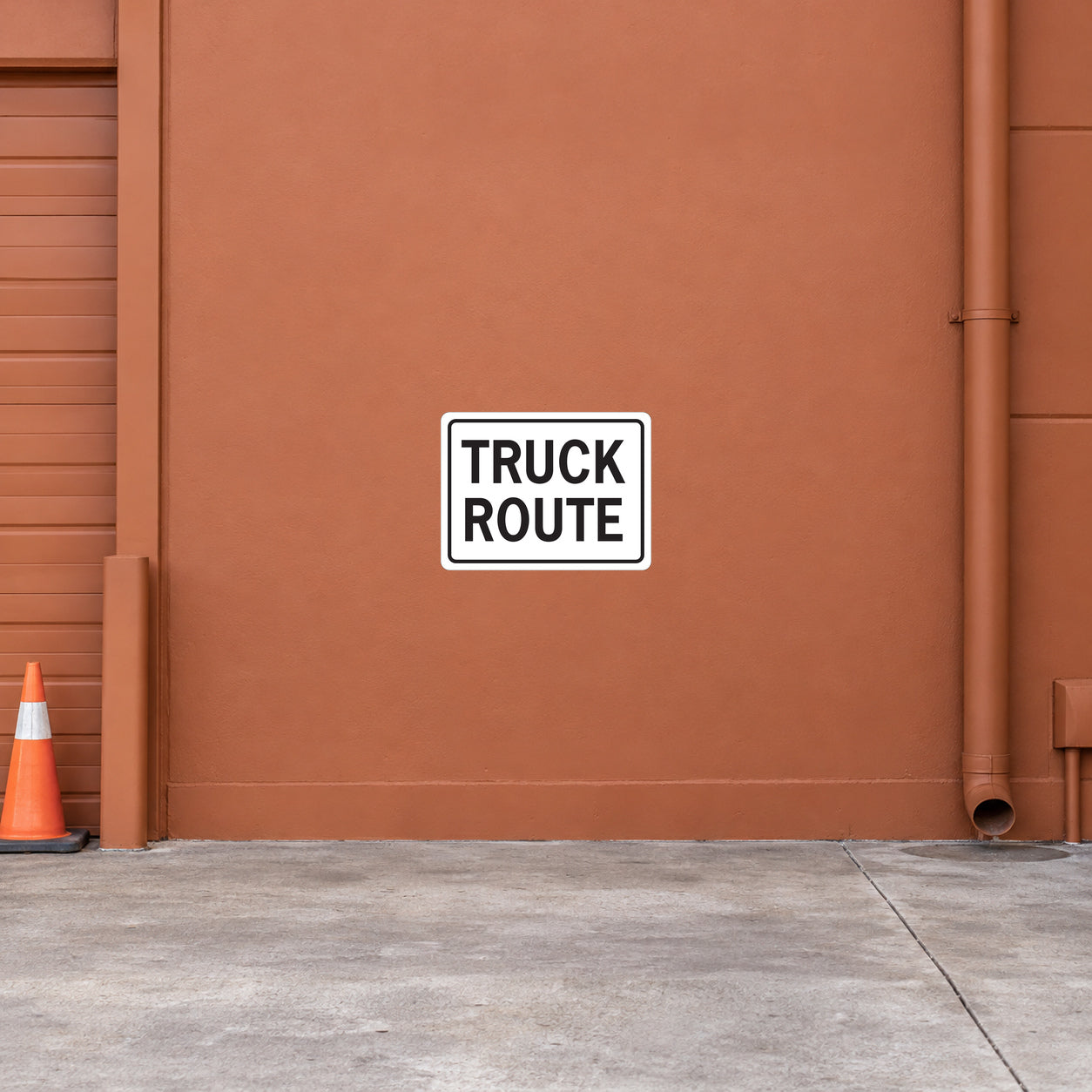Road Sign Sticker applied in a continuous soft terracotta logistics depot wall with traffic cone at far left