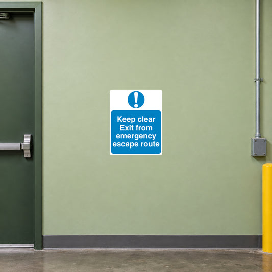Safety Sign Sticker applied in a smooth pale green wall by a rear workshop emergency escape door, clear route below and door frame extreme left