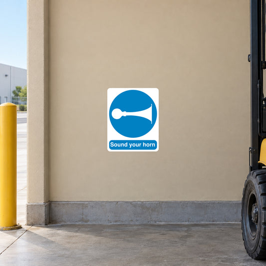 Safety Sign Sticker applied in a smooth light tan warehouse wall beside a vehicle blind corner, forklift wheel cropped extreme right bottom and safety bollard far left