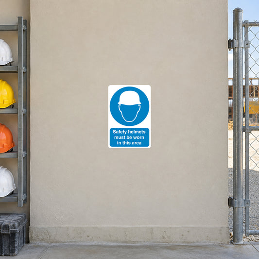 Safety Sign Sticker applied in a smooth pale beige wall at a construction site helmet issue area, hard hats far left and fence gate edge far right