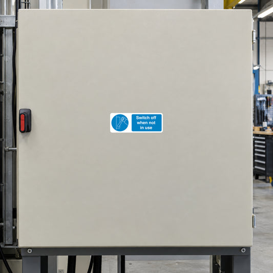 Safety Sign Sticker applied in Large single smooth beige painted machinery control enclosure, isolated switch at extreme left edge, workshop context at far right