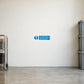 Safety Sign Sticker applied in Pale ivory smooth loading area wall with a clear swept concrete floor, stacked empty bins only at extreme right and goods trolley at extreme left