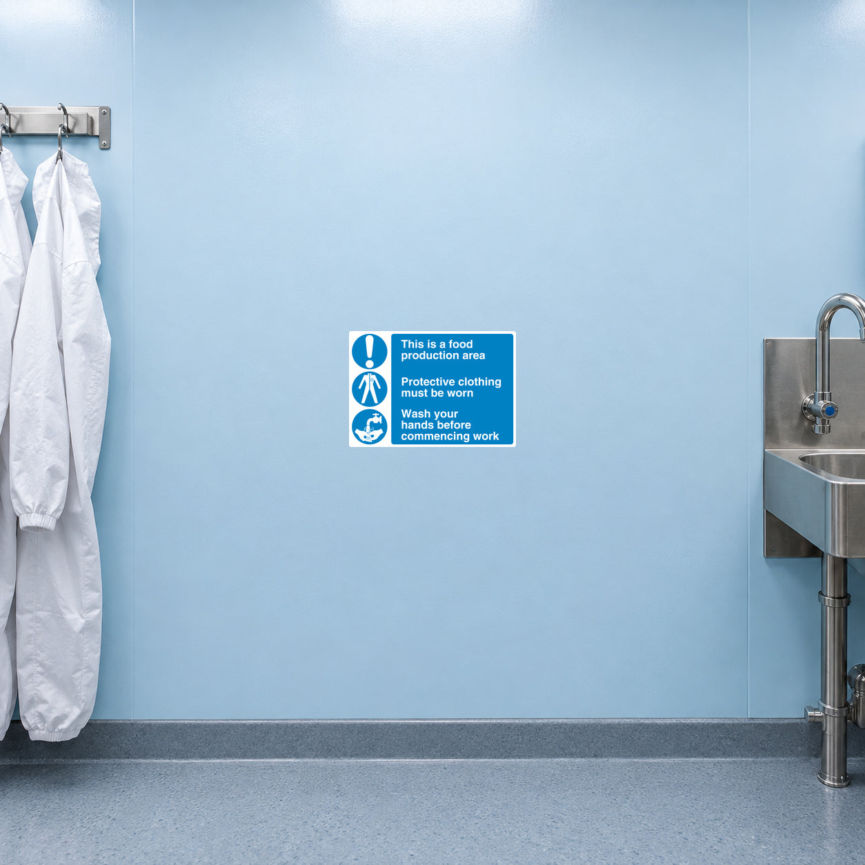 Safety Sign Sticker applied in Smooth pale blue food manufacturing entry wall, clean overalls at extreme left and wash station tap only bottom right below y85%, bright sanitary light