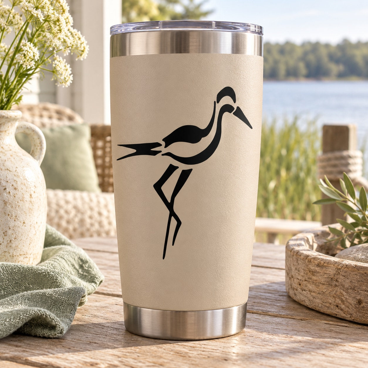 Stainless steel tumbler with black heron decal on beige surface