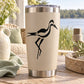 Stainless steel tumbler with black heron decal on beige surface