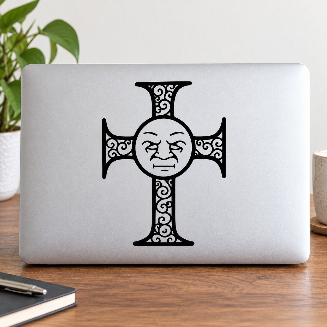Decorative filigree cross decal with face motif on dark laptop lid