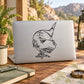 Black line-art T-rex decal on a laptop lid, smiling dinosaur face and snout