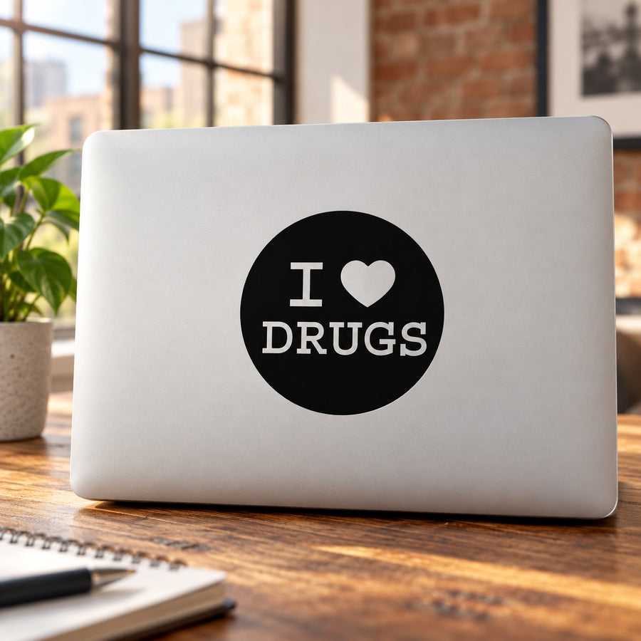 Black circular decal reading "I ♥ DRUGS" on a light laptop cover