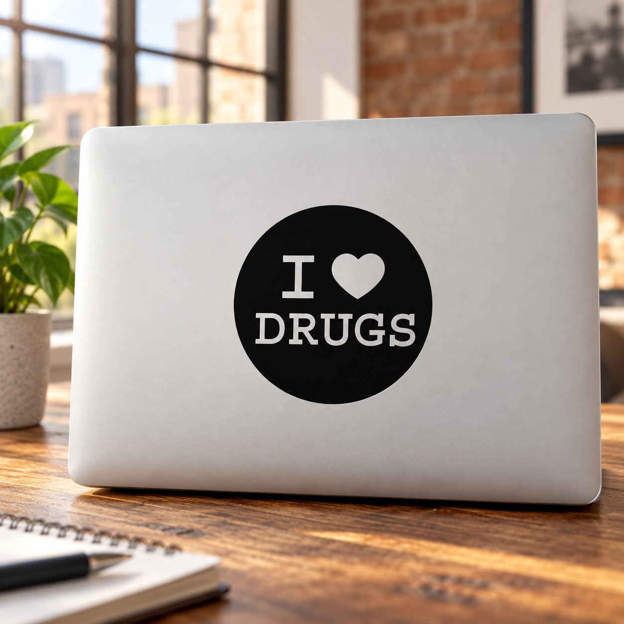 Black circular decal reading "I ♥ DRUGS" on a light laptop cover