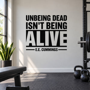 Black typography wall decal: 'UNBEING DEAD ISN'T BEING ALIVE' E.E. Cummings